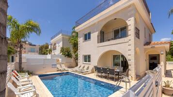 A poolside area with lounge chairs, a dining table, and a two-story building with balconies.