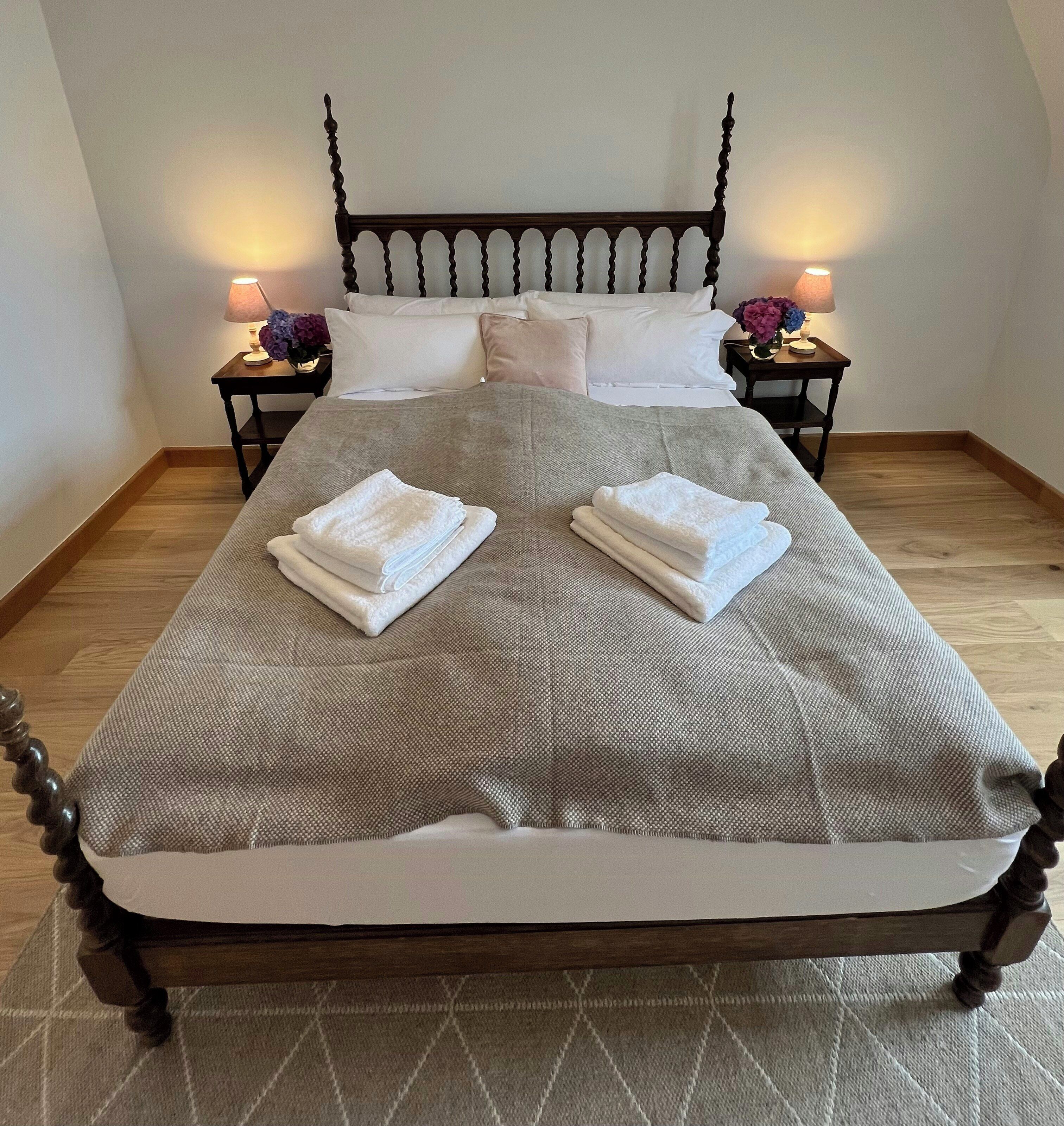 Un lit bien fait, avec une tête de lit, deux tables de chevet avec des lampes et un plancher en bois.