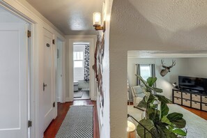 A hallway with a patterned rug, a wall-mounted light fixture, and a television in a living area. - Walkable Family Home in the Heart of Kalispell (Kalispell)