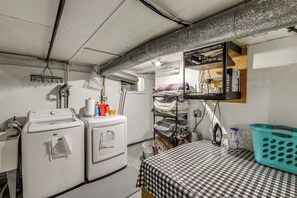 A laundry room with a checkered table, a washing machine, a dryer, a shelf with folded clothes, and a sign indicating the room's purpose. - Walkable Family Home in the Heart of Kalispell (Kalispell)