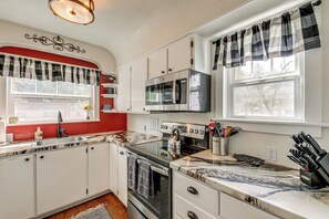 A kitchen with white cabinets, a stainless steel stove, a microwave, and a window with curtains. - Walkable Family Home in the Heart of Kalispell (Kalispell)