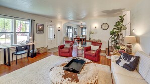A spacious living room with a large window, a dining area, and a cozy seating area with leather chairs and a white sofa. - Walkable Family Home in the Heart of Kalispell (Kalispell)