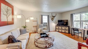 A living room with a sofa, ottoman, TV, and a mounted deer head. - Walkable Family Home in the Heart of Kalispell (Kalispell)