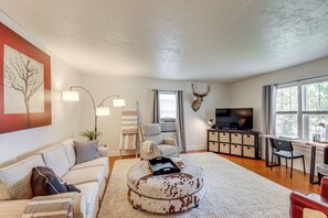 A living room with a sofa, ottoman, TV, and a mounted deer head. - Walkable Family Home in the Heart of Kalispell (Kalispell)