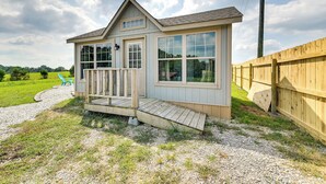 Eine kleine Holzhütte mit Veranda, großen Fenstern und einem Kiesweg, der zu einem blauen Stuhl führt.