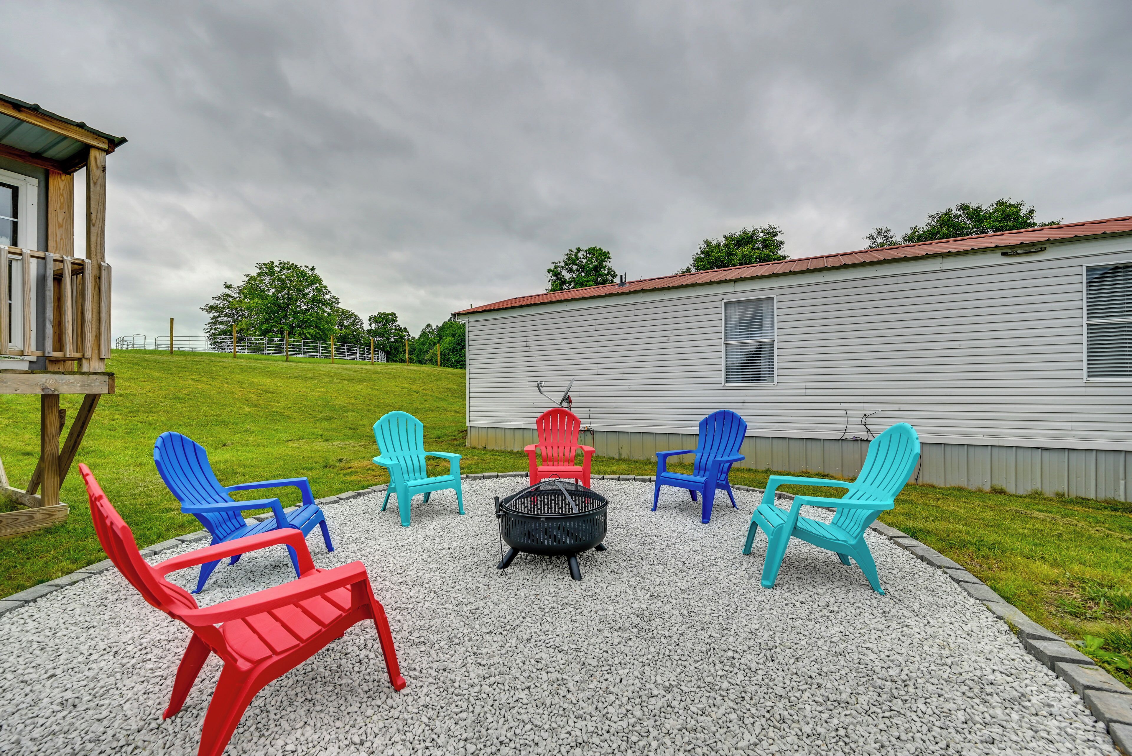 A gravel patio with colorful Adirondack chairs arranged around a black fire pit.