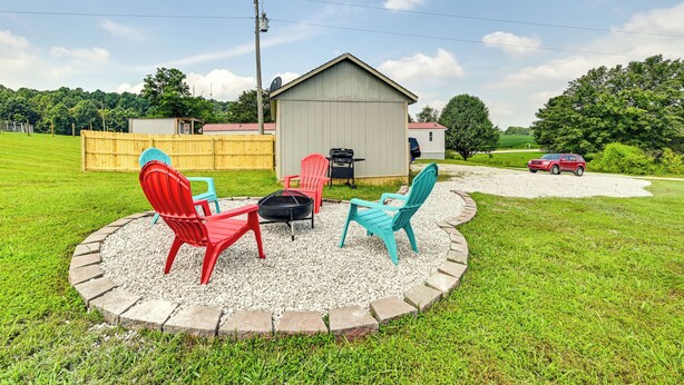 A circular outdoor seating area with four Adirondack chairs, a fire pit, and a small shed in the background. - Countryside Escape w/ Fire Pit By Mammoth Cave! (Brownsville)