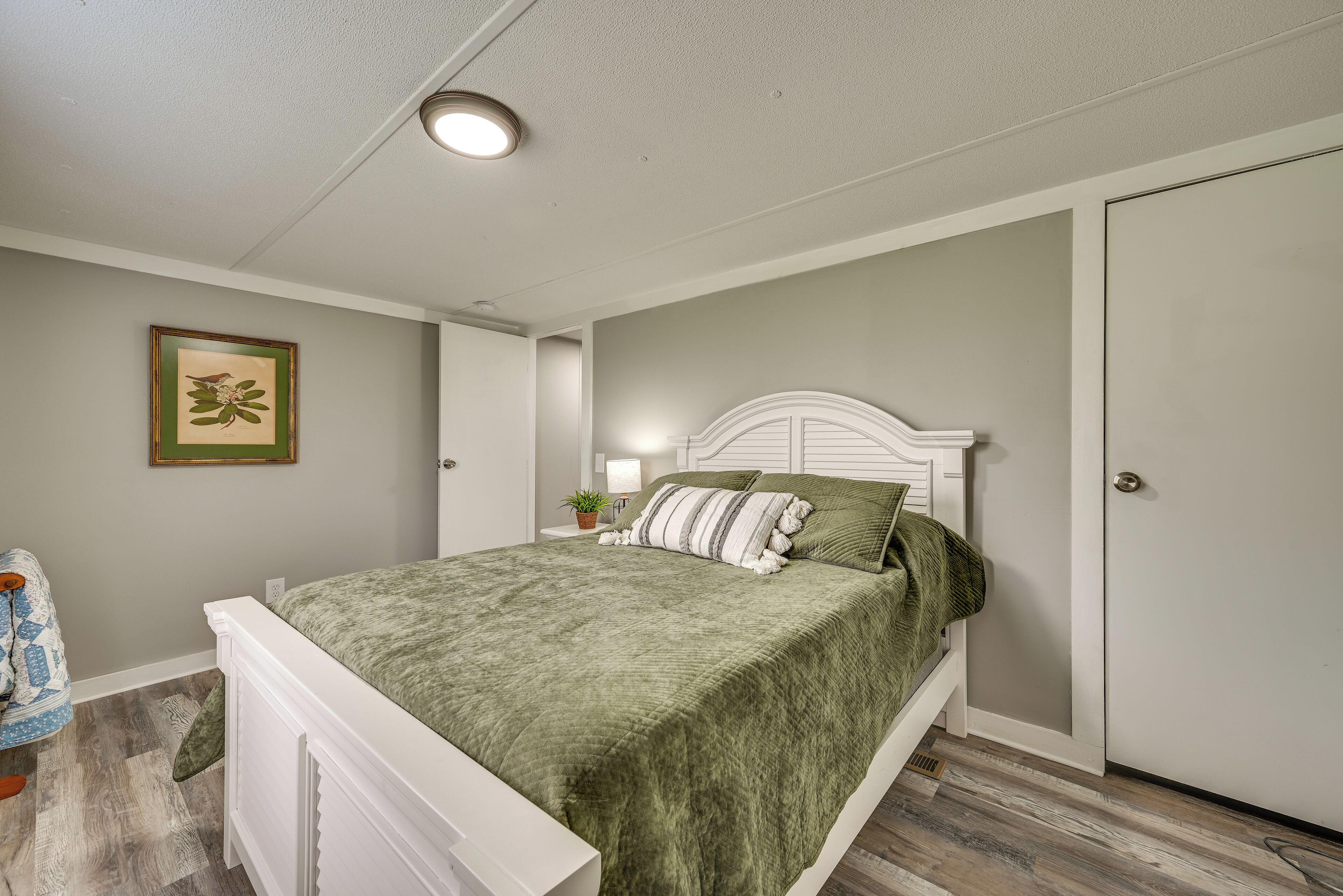 Een slaapkamer met een bed, nachtkastje, lamp, een lijst met foto aan de muur en een deur.