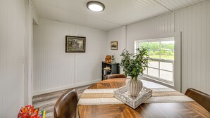 Ein Esszimmer mit Holztisch, Stühlen, einer Vase mit Pflanze, gerahmten Bildern an der Wand und einem Fenster mit Blick.