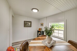Ein Esszimmer mit Holztisch, Stühlen, einer Vase mit Pflanze, gerahmten Bildern an der Wand und einem Fenster mit Blick.