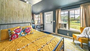Ein Schlafzimmer mit einem Bett, einem Sessel, einem Schreibtisch und einem Fenster mit Vorhängen.