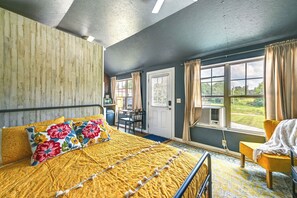Ein Schlafzimmer mit einem Bett, einem Sessel, einem Schreibtisch und einem Fenster mit Vorhängen.