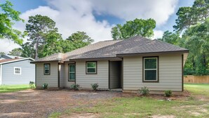 Uma casa térrea com telhado em duas águas, varanda frontal e pequeno jardim da frente com caminho de pedras.