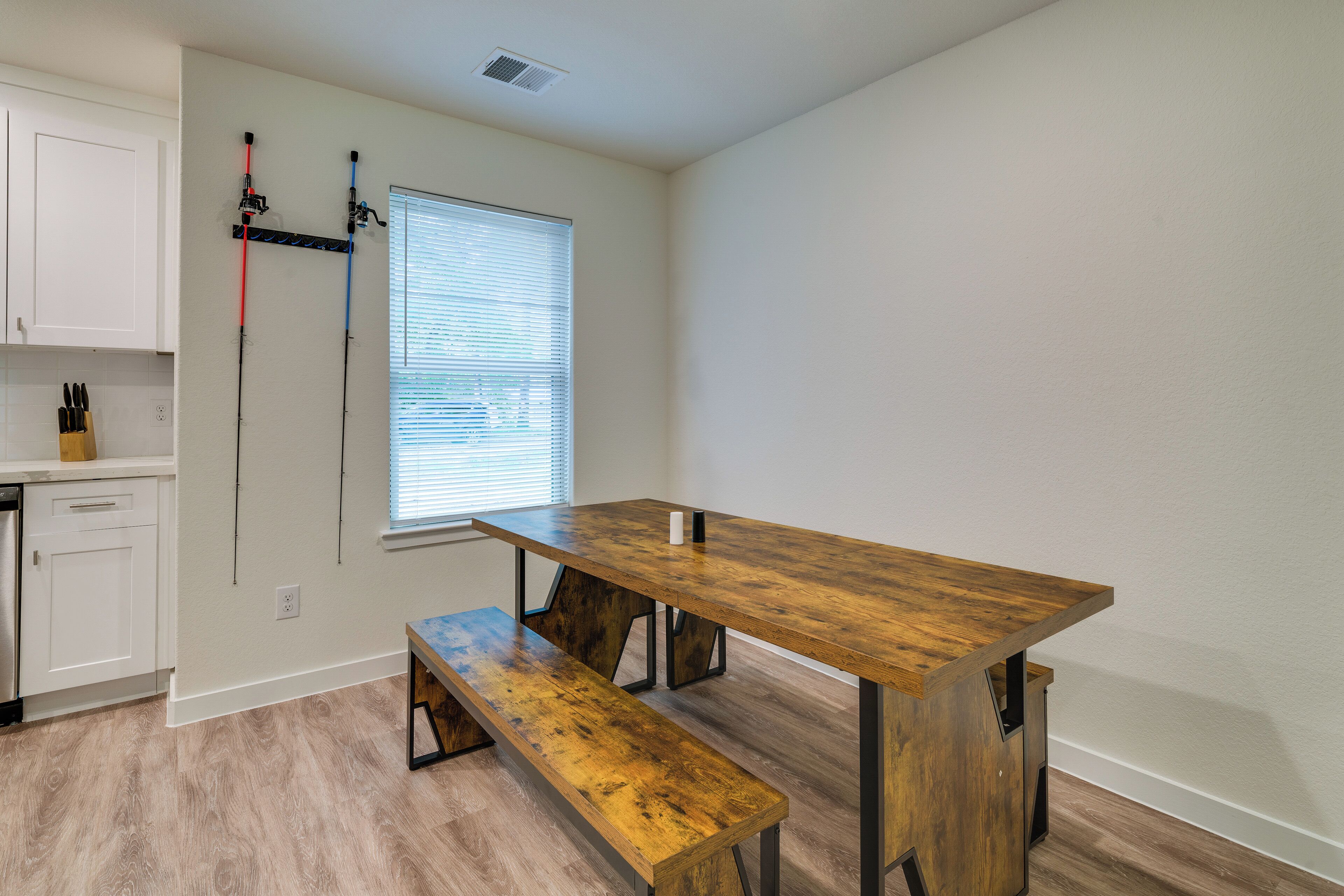 A room with a wooden dining table, bench, white cabinets, and a window with blinds.