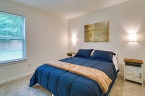 A bedroom with a bed, two bedside tables, a wall-mounted artwork, and a window with blinds.