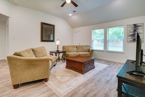 A living room with a sofa, a coffee table, a TV stand, and a ceiling fan. - Piney Woods Escape! Magnolia Home w/ Lake Access (Magnolia)