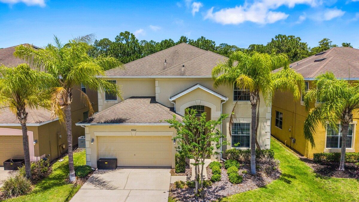 A residential building with a garage, a covered driveway, and a well-maintained lawn with palm trees.