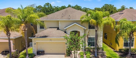 A residential building with a garage, a covered driveway, and a well-maintained lawn with palm trees.