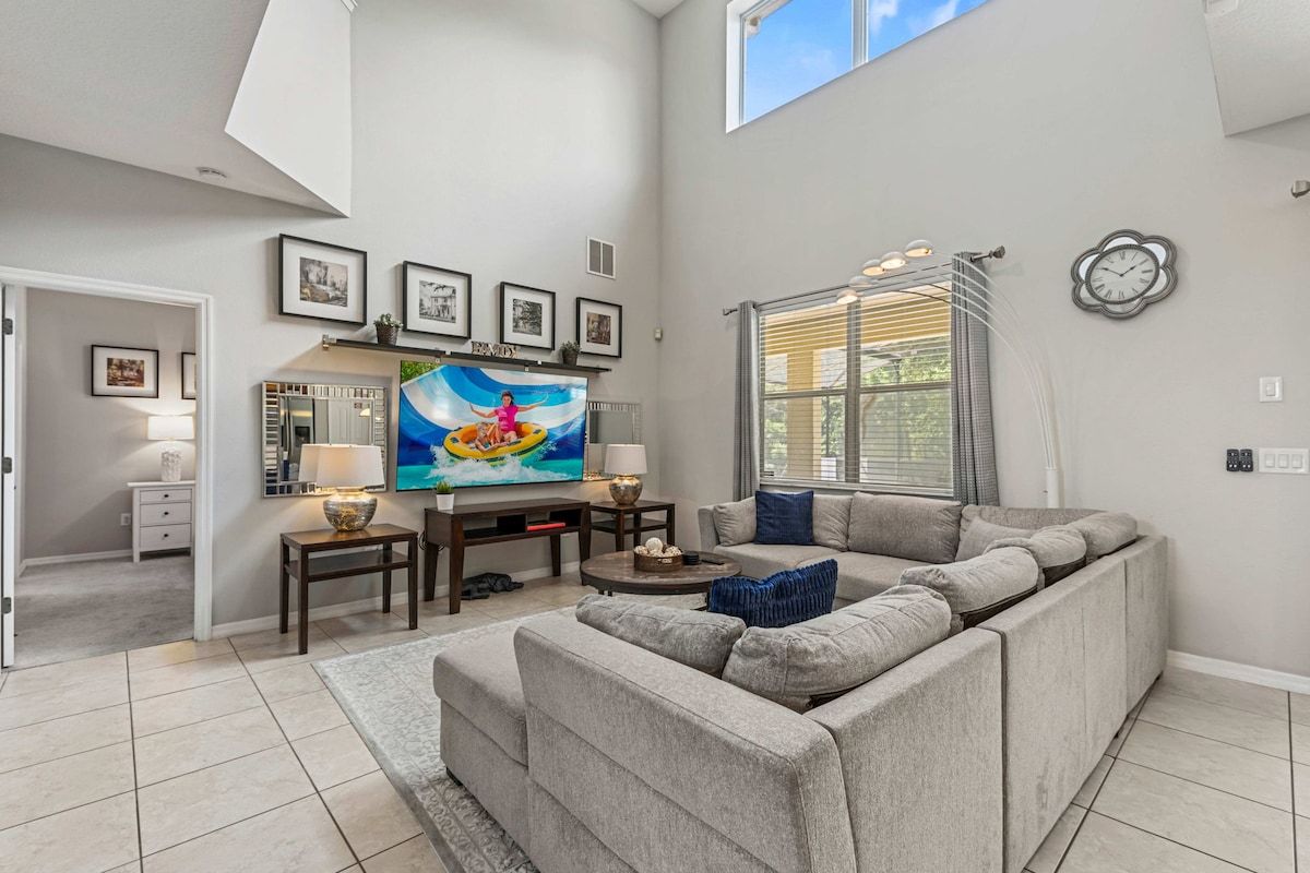 A spacious living room with a large sectional sofa, a flat-screen TV, and a dining area with a table and chairs.