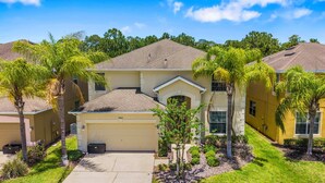 A residential building with a garage, a small driveway, and surrounding palm trees. - Sleeps 13·Pvt Pool+Spa·Game Room·Clubhouse (Kissimmee)