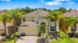 A residential building with a garage, a small driveway, and surrounding palm trees. - Sleeps 13·Pvt Pool+Spa·Game Room·Clubhouse (Kissimmee)