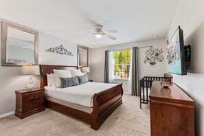 A bedroom with a bed, nightstand, dresser, ceiling fan, window with curtains, and artwork on the wall. - Sleeps 13·Pvt Pool+Spa·Game Room·Clubhouse (Kissimmee)