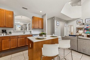 A modern kitchen with wooden cabinets, a central island, and bar stools. - Sleeps 13·Pvt Pool+Spa·Game Room·Clubhouse (Kissimmee)