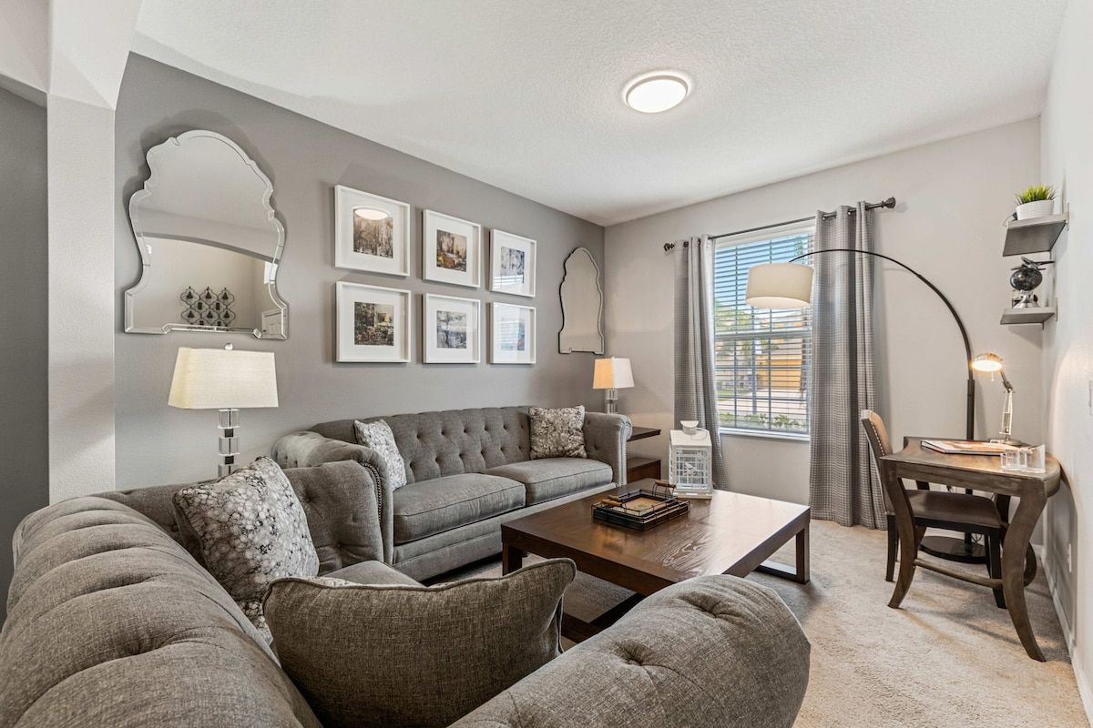 A modern living room with a grey sofa set, a wooden coffee table, and a dining area with a small table and chairs.