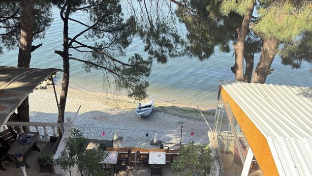Uma área de pátio com mobiliário externo, um barco na costa e vista para a água.