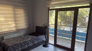 Quarto com cama, ventoinha, radiador e vista exterior por uma porta de correr de vidro.