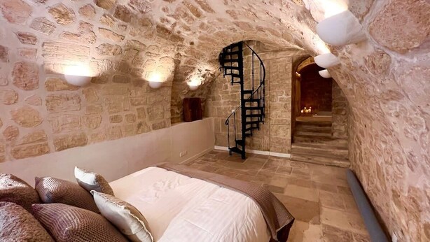 A stone-walled room with a bed, a spiral staircase, and a view of a lower level. - Serenity :  Meditation at Notre - Dame — AC (Paris)