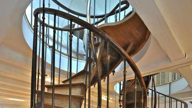 Una escalera de caracol con detalles de madera y barandillas de metal, que conduce a un nivel superior.