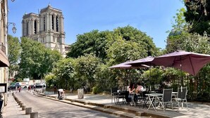 Una calle con mesas al aire libre, un edificio histórico al fondo y árboles.
