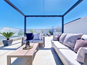 Eine Dachterrasse mit Glastdeckung, einer Couch, einem Couchtisch und Kübelpflanzen.