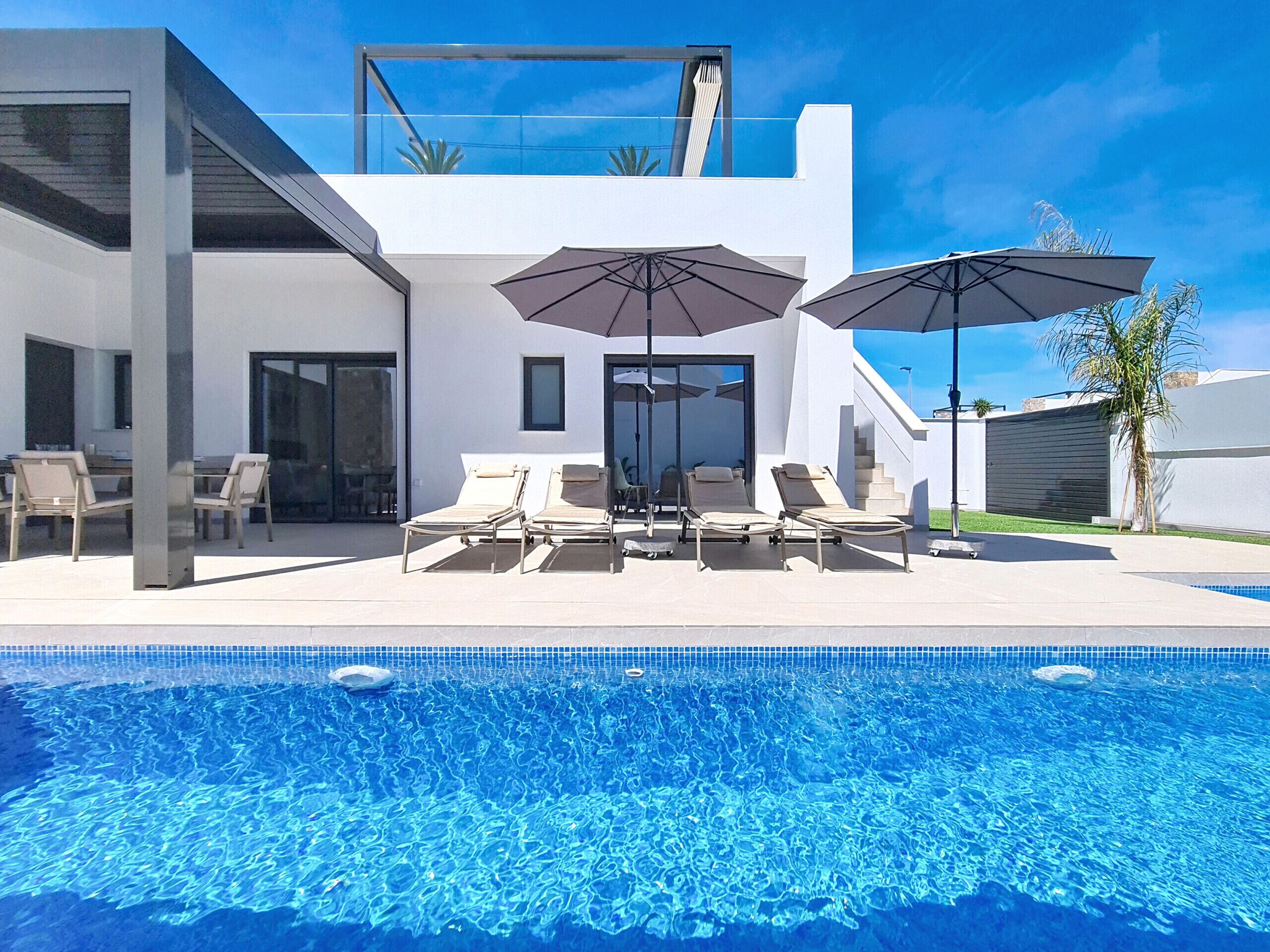 Una casa moderna con piscina, tumbonas y sombrillas.