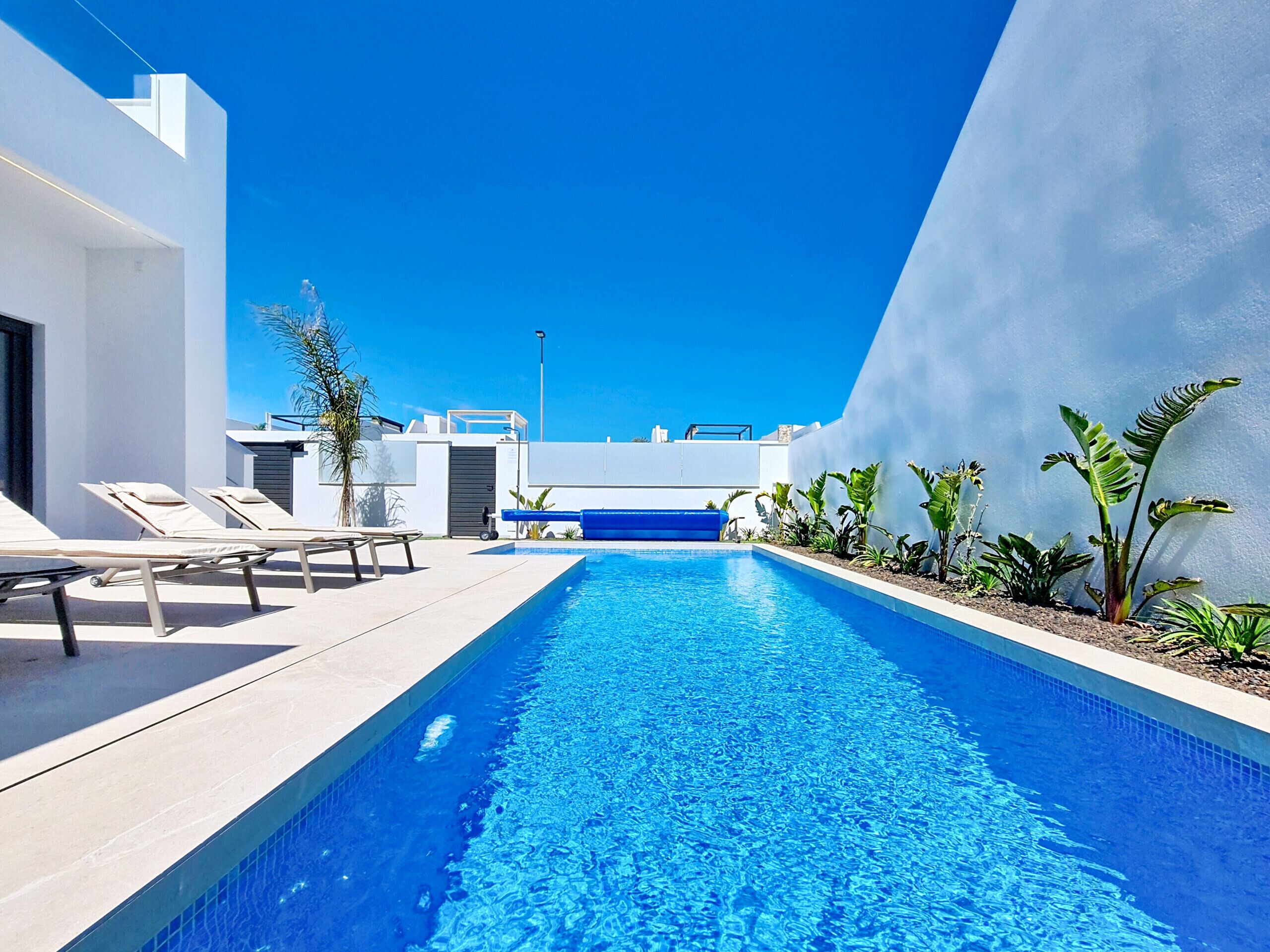 A modern pool area with lounge chairs, a clear blue pool, and a white building with a blue accent wall.