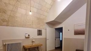 A spacious room with a high ceiling, a wooden floor, a brown sofa, a small table, and a radiator. - B&B Luna Rossa (Altamura)