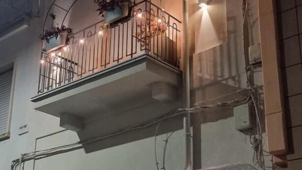 A building with a balcony with potted plants and string lights, a wooden door, and a number '73' sign. - B&B Luna Rossa (Altamura)