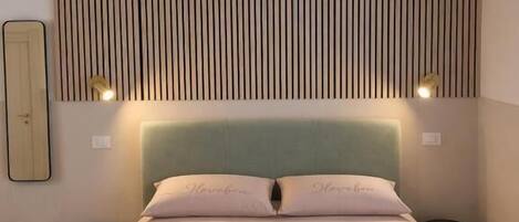 Une chambre d’hôtel avec un lit, une tête de lit à lattes verticales, deux lampes de chevet et un miroir au mur.