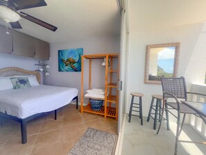 Ein Schlafzimmer mit Bett, einer Holzregaleinheit, einem Sessel und Blick aufs Meer.