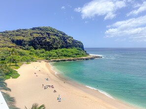 Ein Strand mit klarem türkisblauem Wasser, einem sandigen Ufer und einem üppigen, grünen Hügel im Hintergrund.