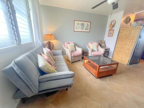 Ein Wohnzimmer mit grauem Sofa, zwei Sesseln, einem Couchtisch und einem Deckenventilator.