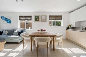 Ein modernes Wohnzimmer mit Sofa, Esstisch, Stühlen, einer Küchenzeile und gerahmten Bildern an der Wand.