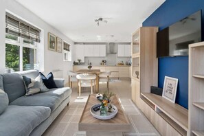 Ein modernes Wohnzimmer mit einem grauen Sofa, einem Couchtisch mit Dekoration und einem Essbereich mit weißem Tisch und Stühlen.
