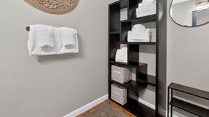 A bathroom with a towel rack, a mirror, a dark wooden shelf with folded towels, and a decorative wall piece. - 404 Doc Susie home Delightful and renovated home, walk to downtown, mt views (Fraser)
