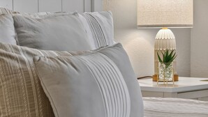 A neatly made bed with pillows, a bedside lamp, and a small plant on a white nightstand. - 404 Doc Susie home Delightful and renovated home, walk to downtown, mt views (Fraser)