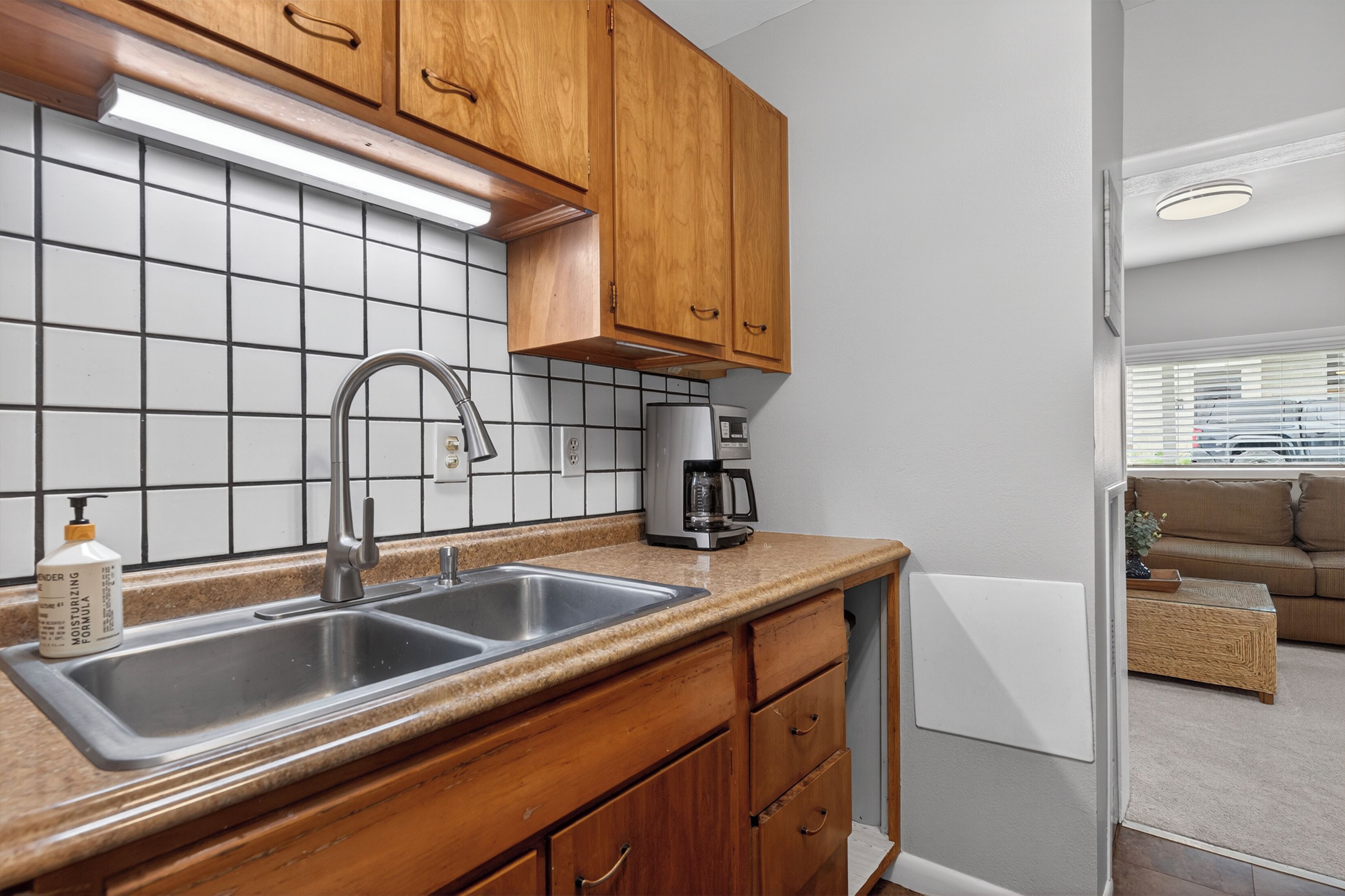 A kitchen with wooden cabinets, a stainless steel sink, a coffee maker, and a tiled backsplash.