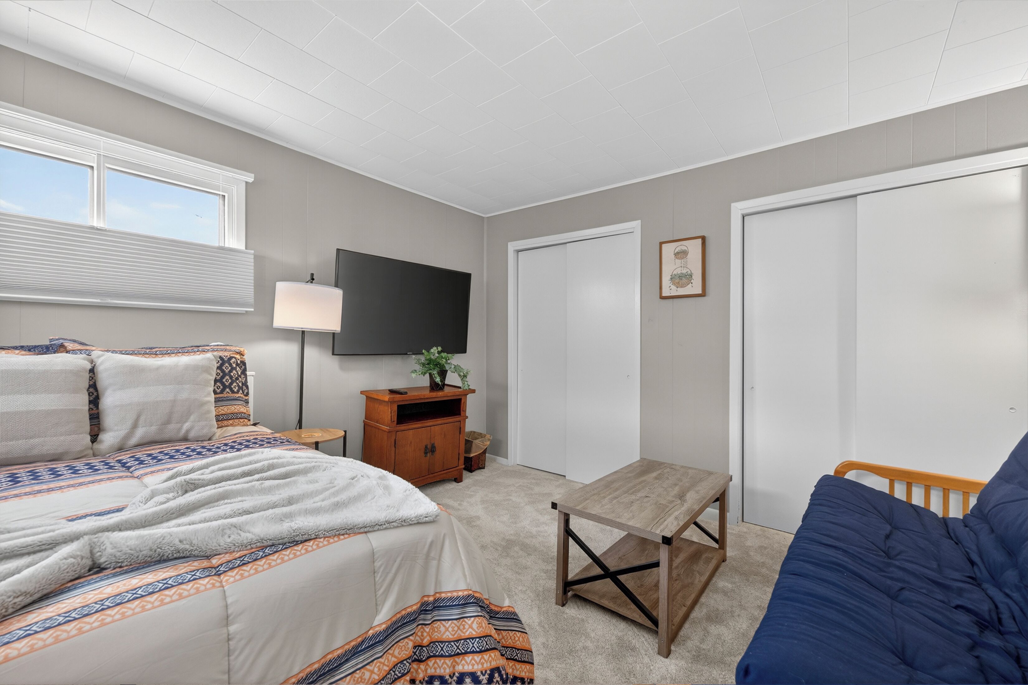 A bedroom with a bed, a TV, a wooden table, and a blue couch.