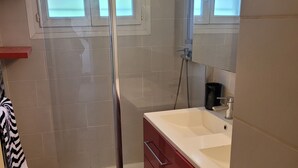Un baño con cabina de ducha de vidrio, un lavamanos blanco, armarios rojos y una alfombra de baño roja.