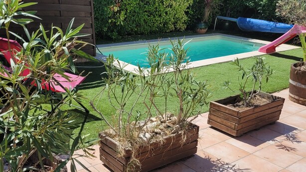 Zona junto a la piscina con plantas en macetas, una valla de madera y una vista despejada del agua.